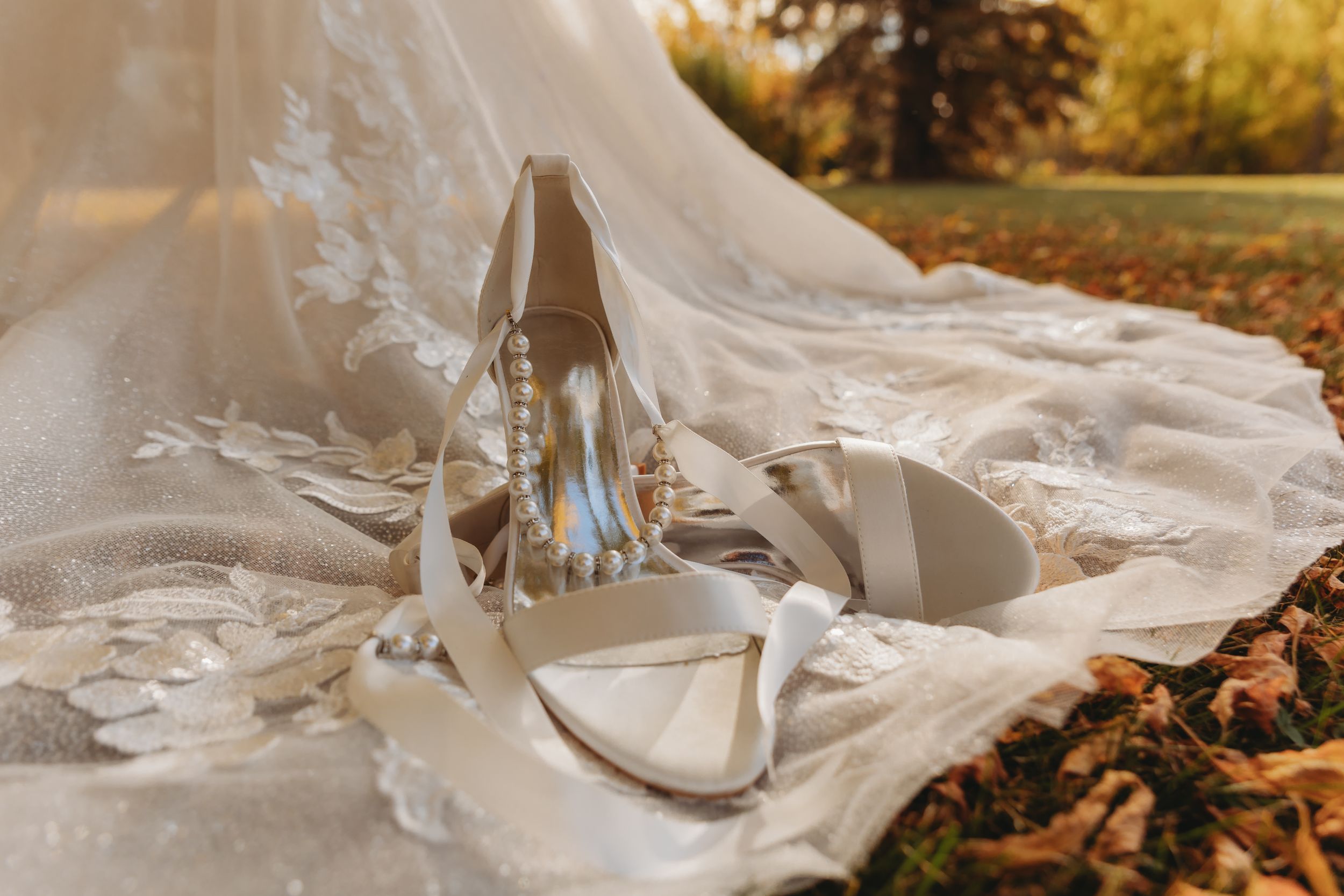 Elegant bridal shoes displayed on lace wedding dress against autumn leaves.
