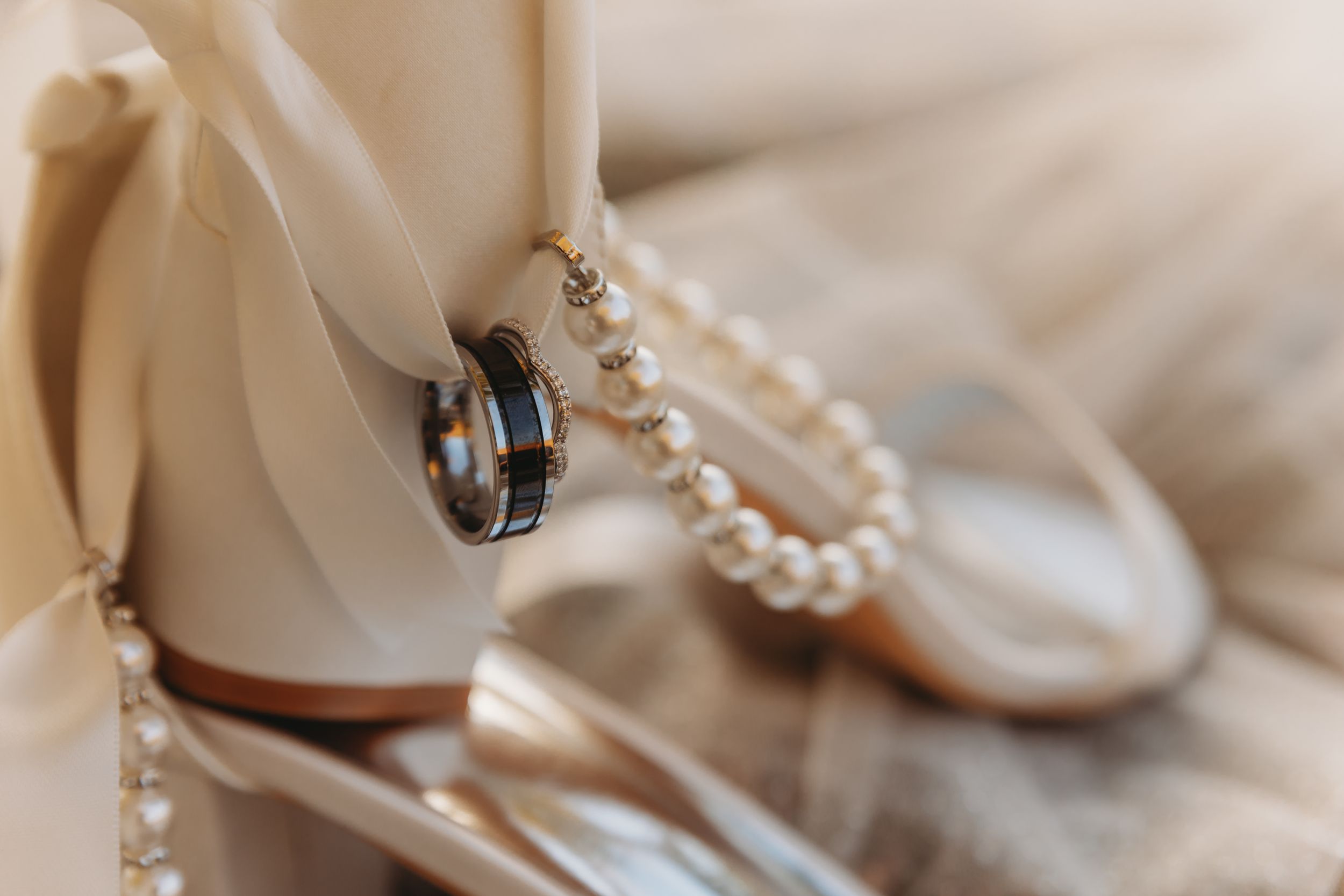 Wedding accessories featuring pearl necklace and rings on white fabric.