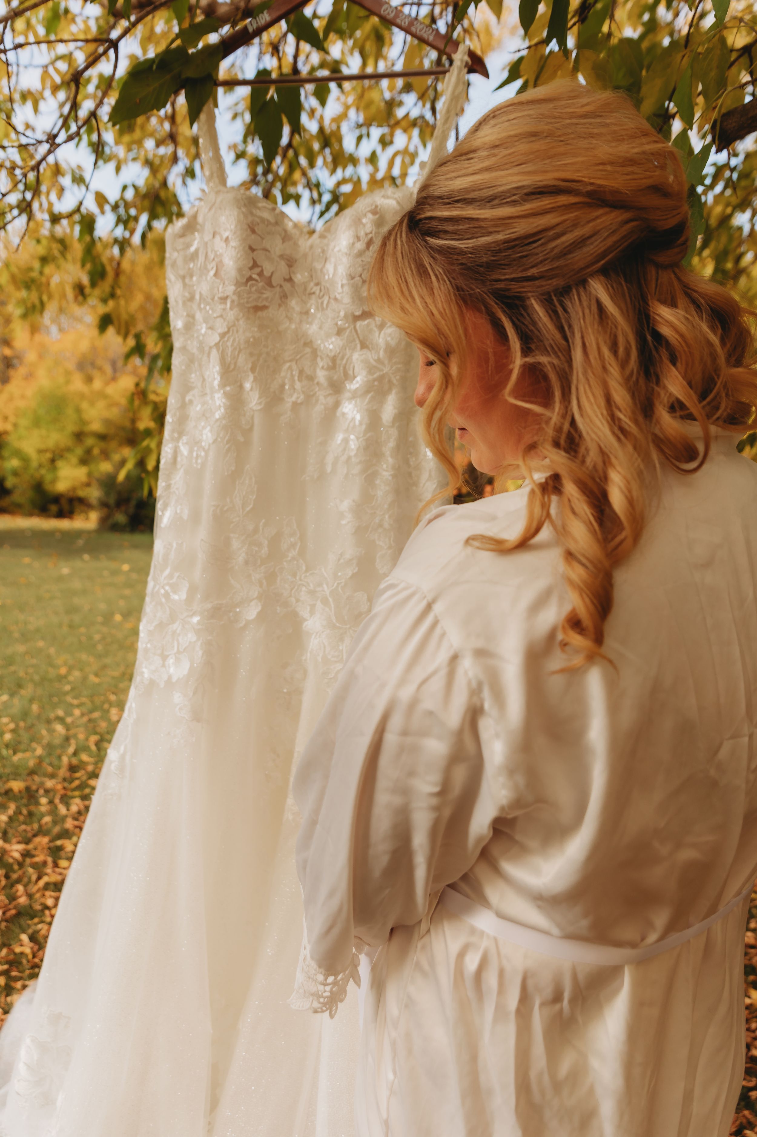 Wedding dress hanging outdoors with autumn foliage in background.