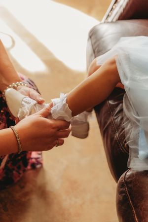 Helping put on delicate white shoes with pearl details during wedding preparations.