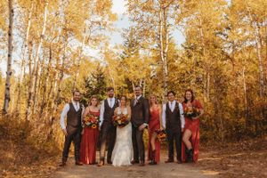 A wedding party poses on a path surrounded by golden autumn trees.