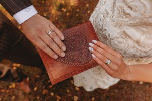 Hands holding an ornate leather-bound book during an autumn wedding ceremony.