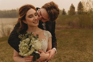 Tender moment with white floral bouquet against rustic outdoor backdrop.