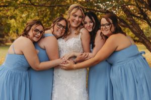 Bridesmaids in light blue dresses embrace the bride in a joyful group photo.