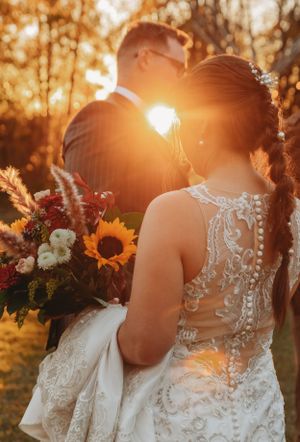 Sunset wedding photo with intricate lace dress and autumn bouquet featuring sunflowers in golden light.