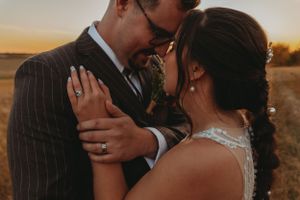 Intimate sunset wedding portrait showing detailed lace dress and pinstripe suit in warm lighting.