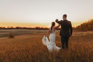 Romantic sunset silhouette of newlyweds walking through golden wheat field.
