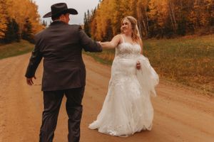 Couple shares romantic moment on dirt road lined with golden fall foliage.