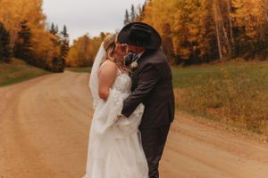 Wedding couple embraces on rustic dirt path with fall colors in background.