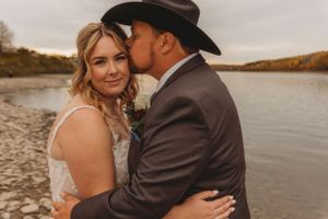 Romantic lakeside moment between newlyweds during autumn sunset.