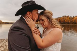 Tender lakeside embrace between newlyweds with autumn foliage backdrop.