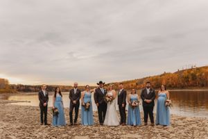 Wedding party poses by lakeside with bridesmaids in blue dresses against fall scenery.