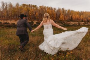 A couple dances joyfully in a field surrounded by golden autumn trees and tall grass.