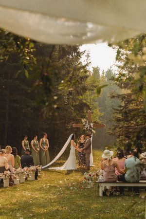 Scenic outdoor wedding ceremony in a forest clearing with wooden benches and evening sunlight.