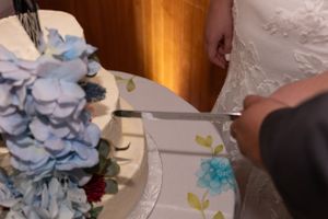 Close-up of a wedding cake with blue floral decorations being cut.