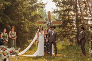 Wedding party celebrates in a rustic outdoor ceremony with evergreen trees and white floral decorations.