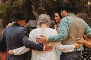 Group hug captured in warm intimate moment at outdoor wedding celebration.