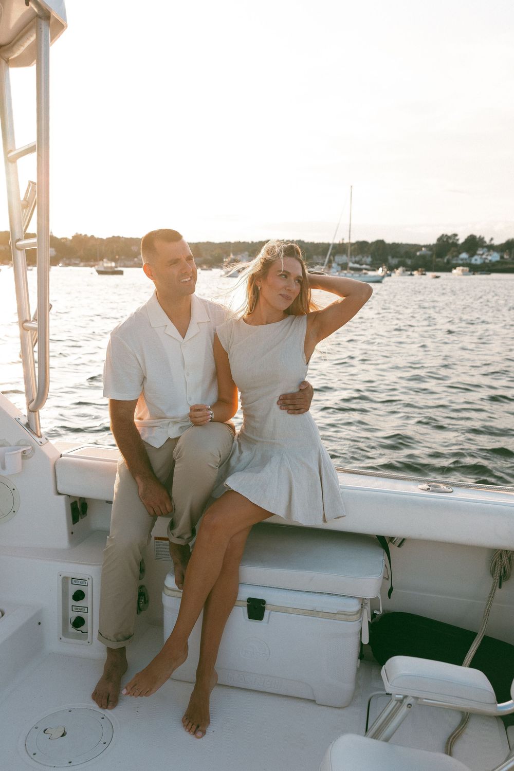 Couple relaxing on deck of white boat during golden hour.