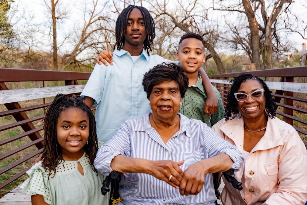 A multigenerational Black family portrait featuring a grandmother in a wheelchair with children on a bridge.
