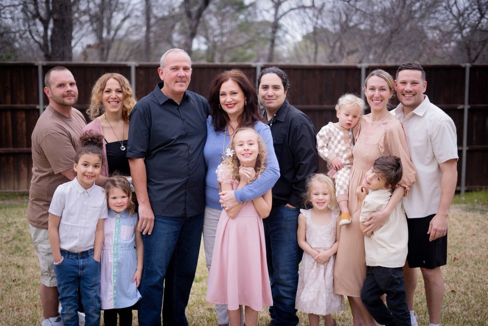 A large extended white family with young children poses together outdoors near a wooden fence in winter.