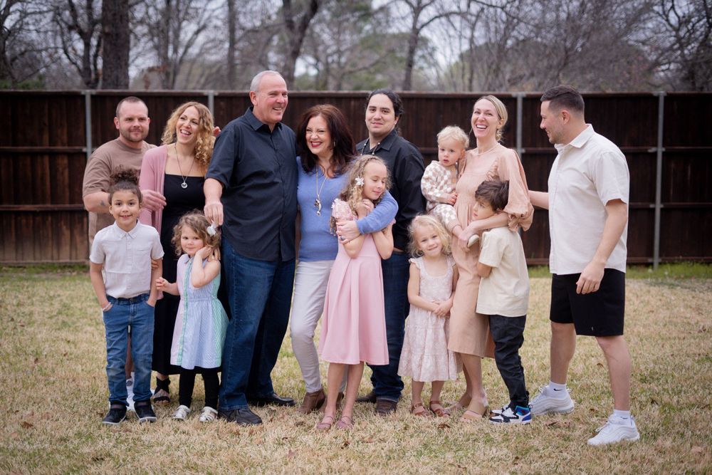 A cheerful multigenerational family laughs together on a lawn with a wooden fence backdrop in winter.