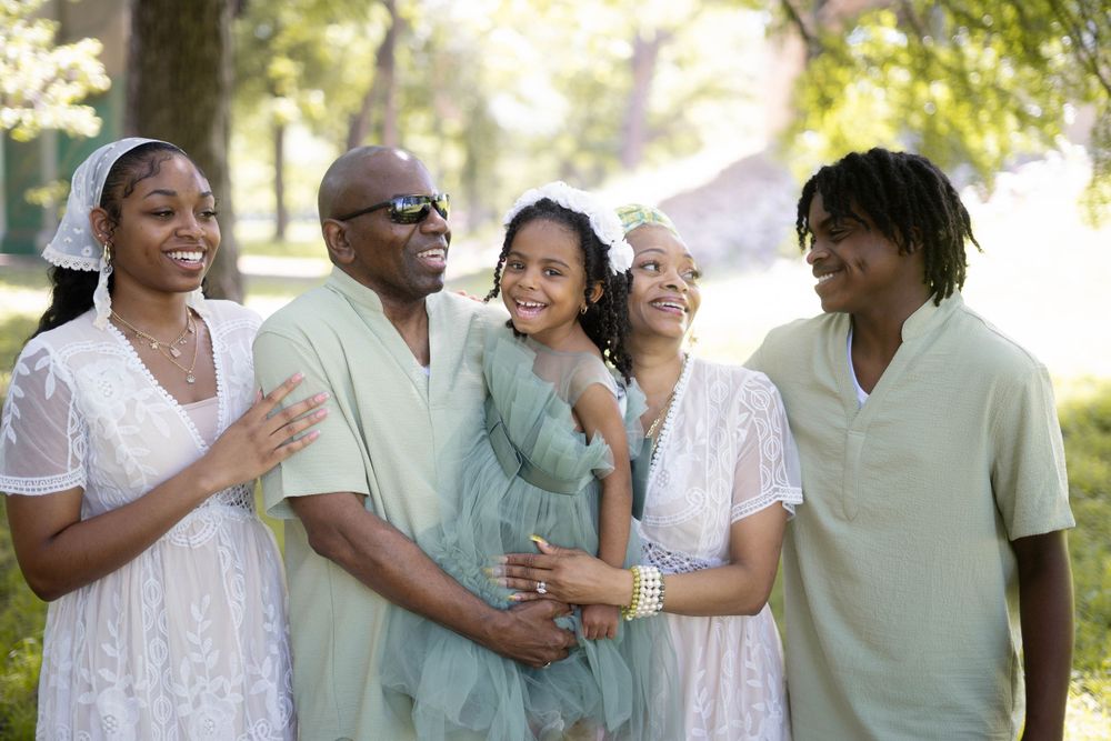 Joyful family of five in coordinated mint and white outfits laughing together in a sunny park setting.