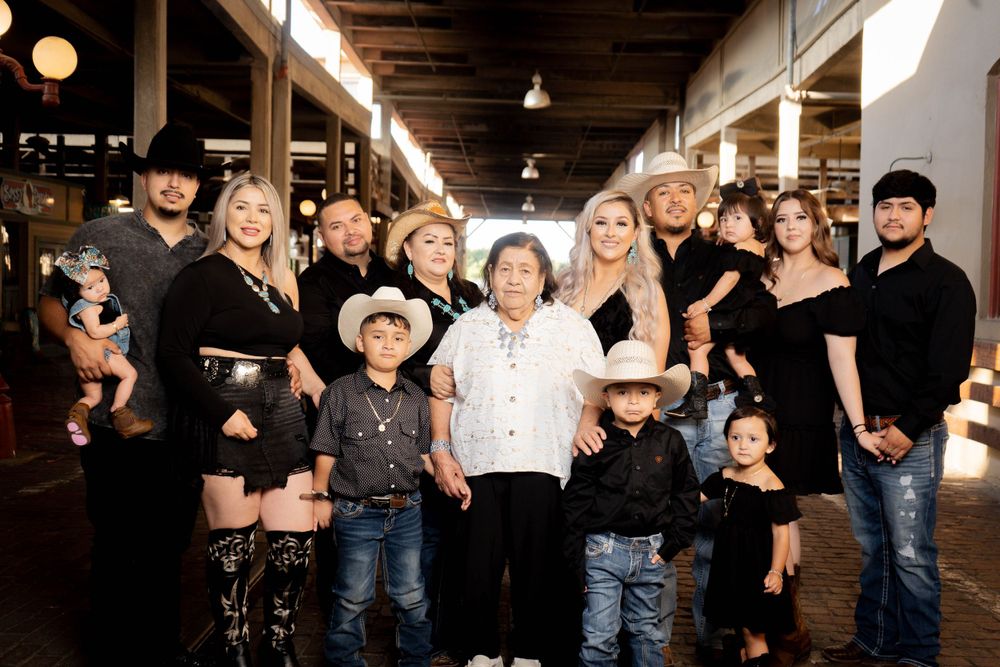 Large family group portrait in western wear posing together in an indoor venue with string lights.