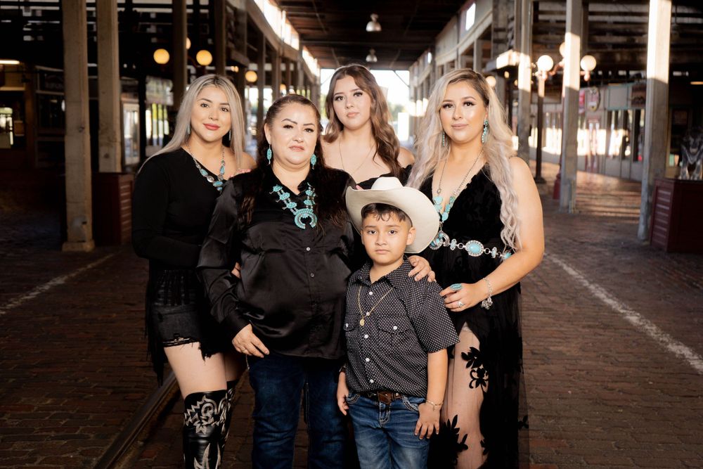 Woman with four family members including a boy in cowboy hat posing in black outfits in a rustic venue.
