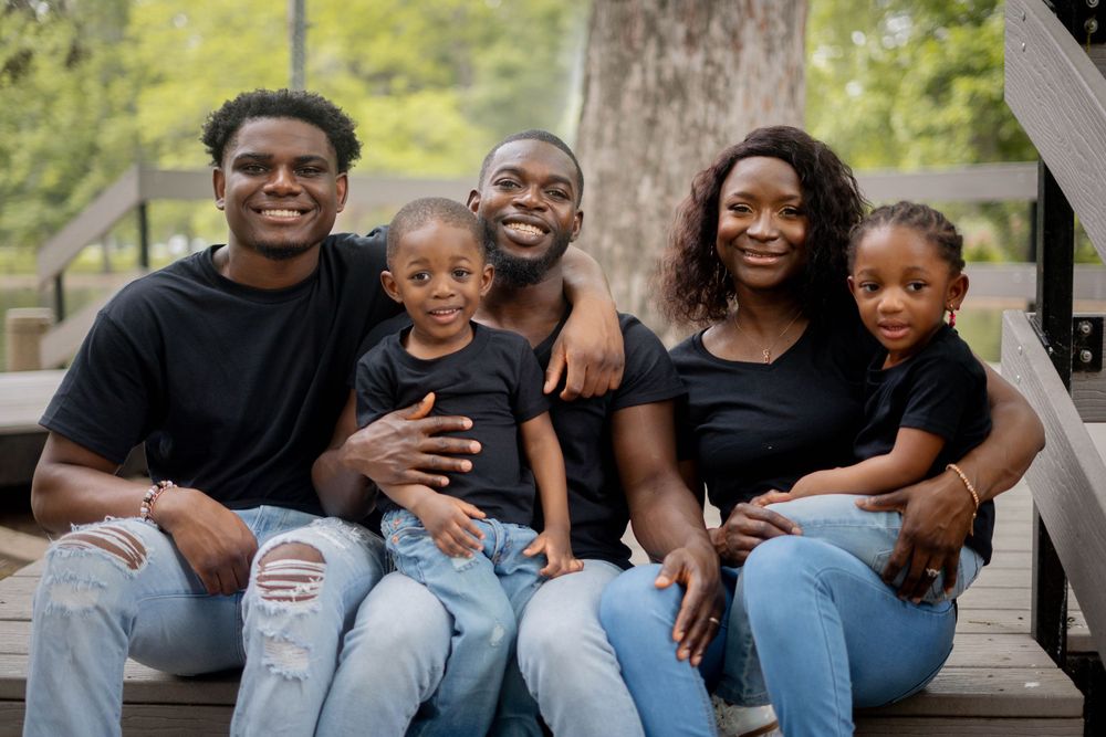 Family of five in matching black outfits sitting together on outdoor steps smiling for a portrait.