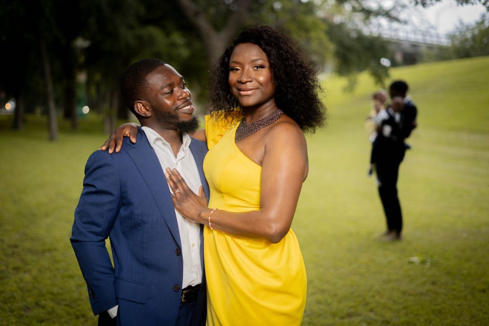 Couple in yellow dress and blue suit sharing a romantic moment on a green lawn at an outdoor event.