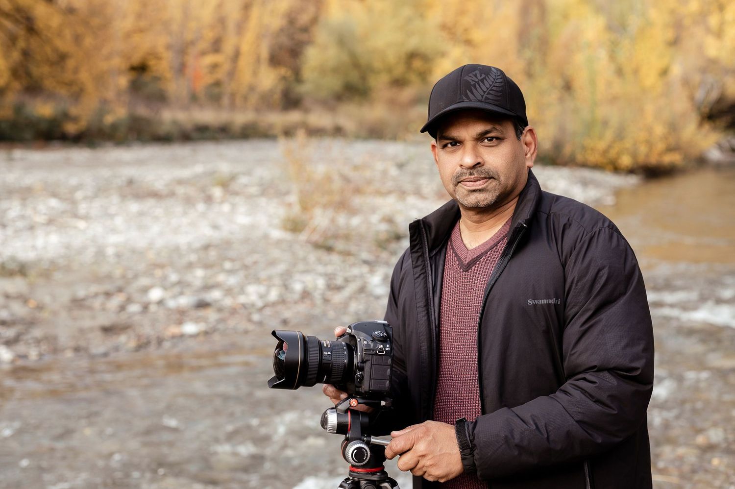Portrait of photographer with professional camera gear in outdoor autumn setting.