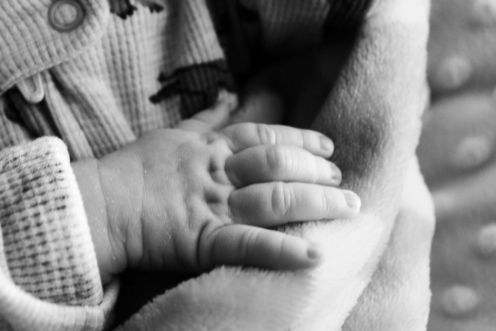 Close-up sequence showing a baby's tiny hand reaching out and grasping an adult's finger in black and white.