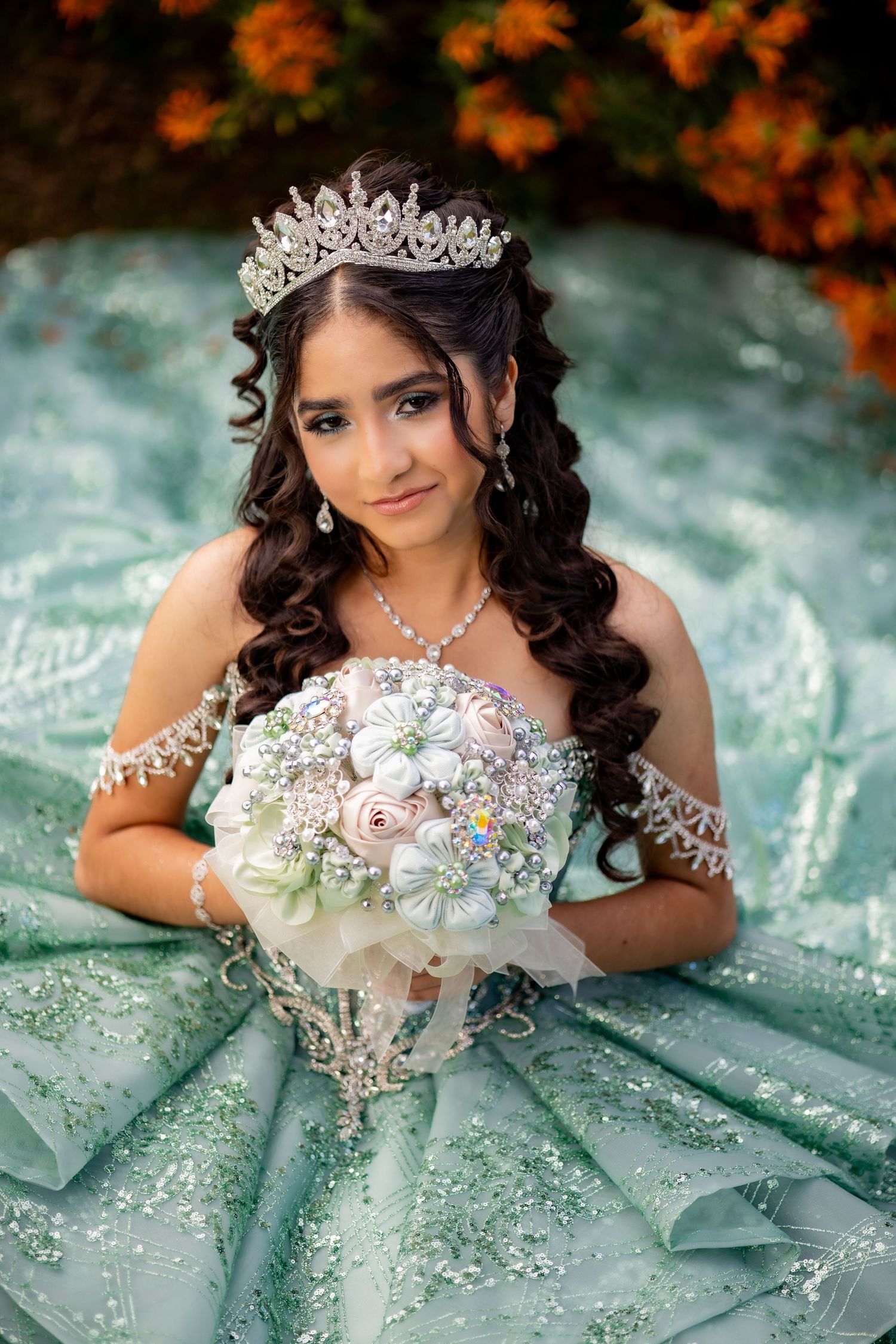 Young woman in pink quinceañera gown wearing silver crown holds colorful bouquet while posing on grass.
