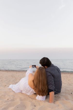 pregnant couple looking at their ultrasound as they lay on the beach