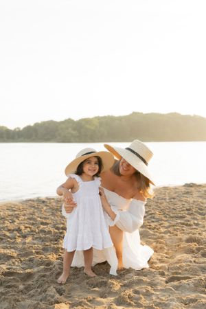 mother and daughter wearing matching hats on the beach and smiling at each other