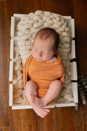 newborn baby boy wrapped in an orange huck Finn swaddle