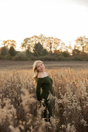 Dreamy outdoor senior photos in a golden field at sunset with soft natural lighting and dried plants in the foreground in the winter