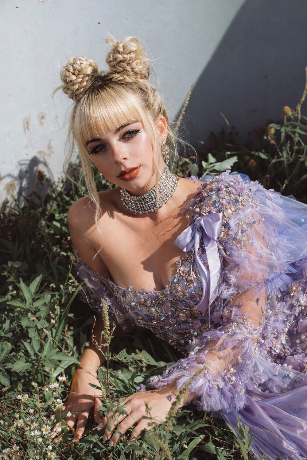 Young woman in lavender beaded tulle gown with double bun hairstyle and choker necklace posing in garden greenery.