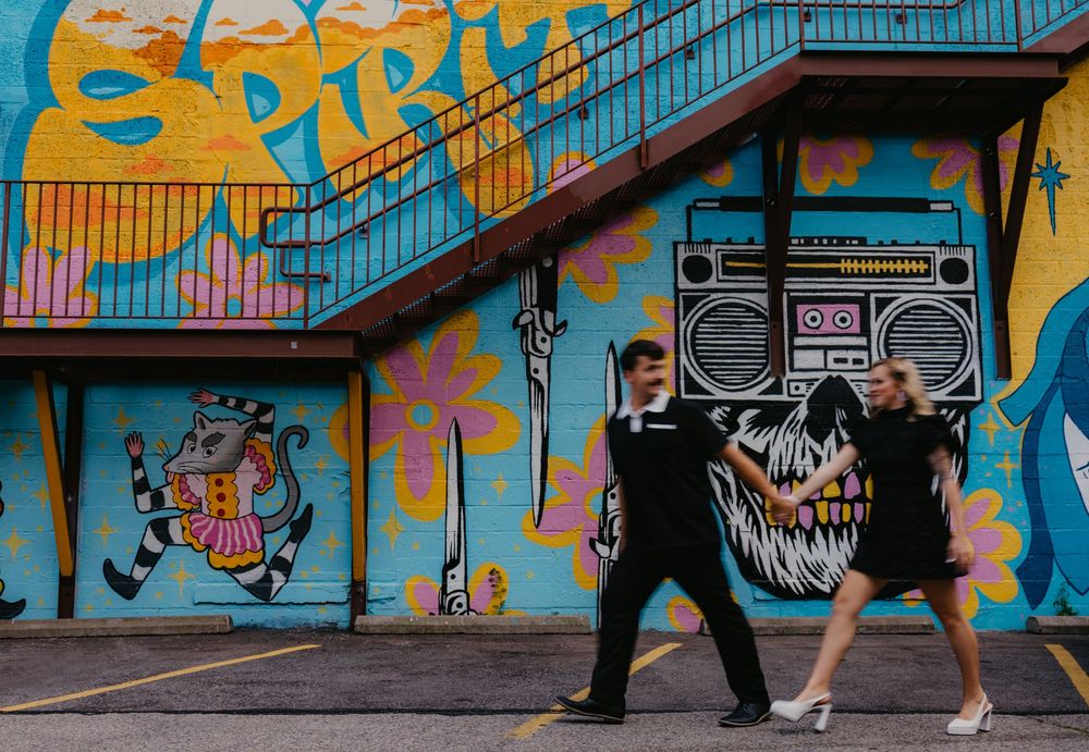 Couple walking in front of colorful graffiti mural with boombox art on urban building exterior.