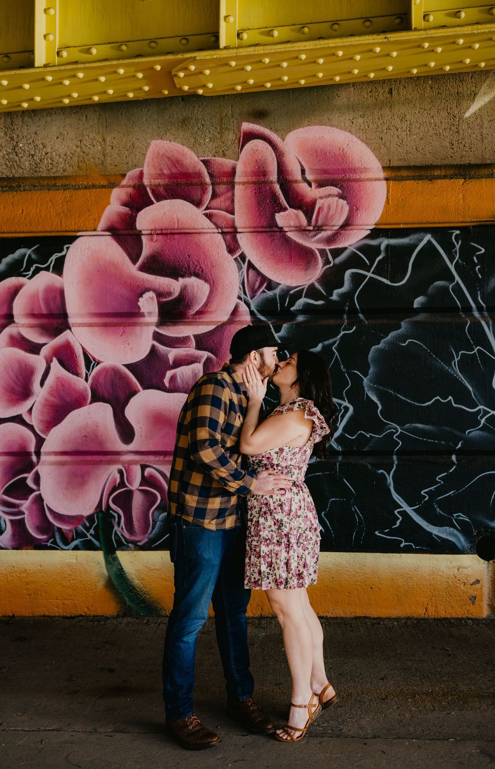 Couple kissing in front of a colorful floral graffiti mural wall.