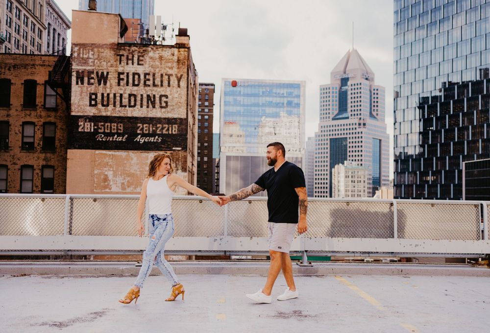 Couple holding hands on rooftop parking garage with New Fidelity Building and Cincinnati skyline backdrop.