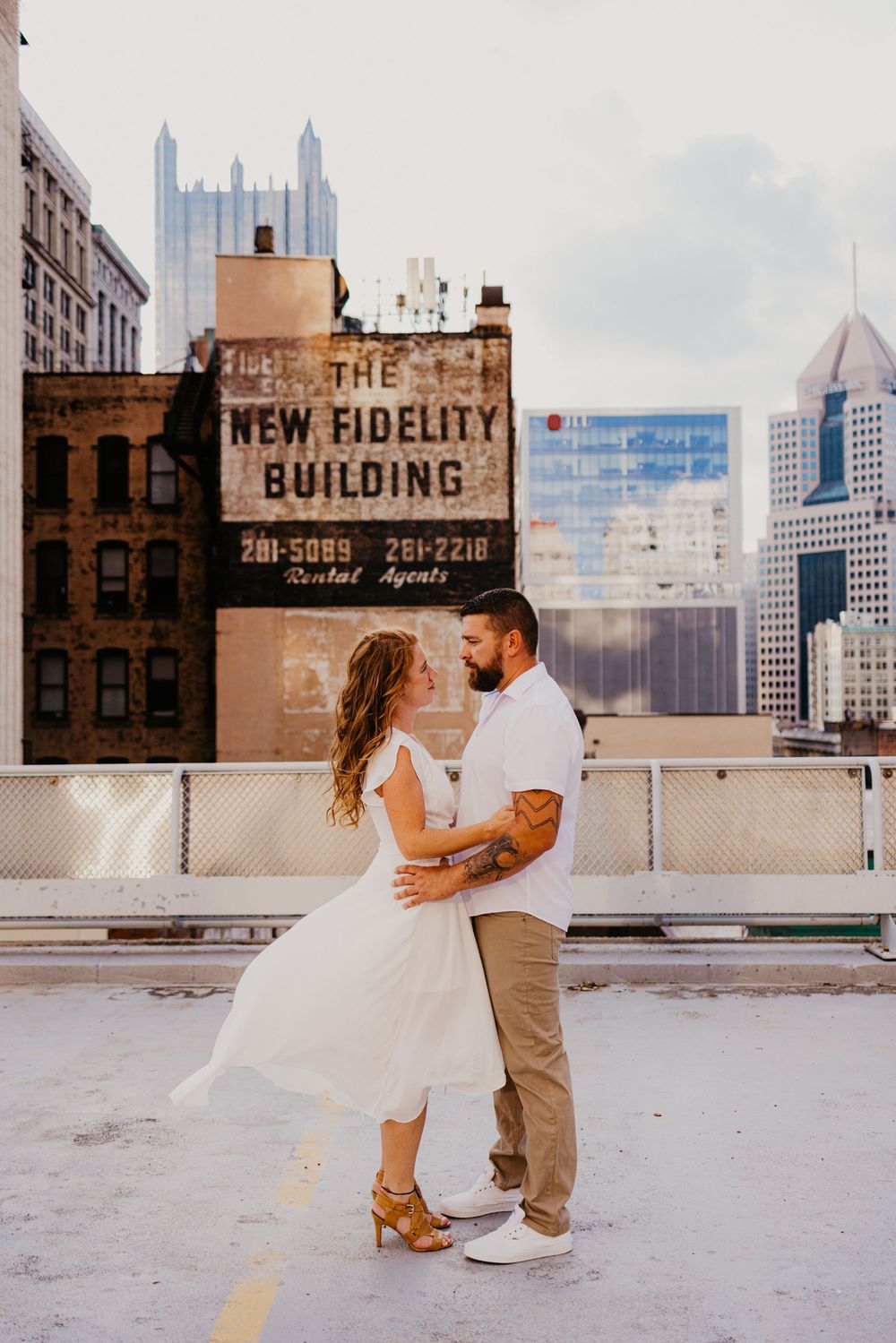 Couple dancing on rooftop with Pittsburgh skyline and New Fidelity Building in background.