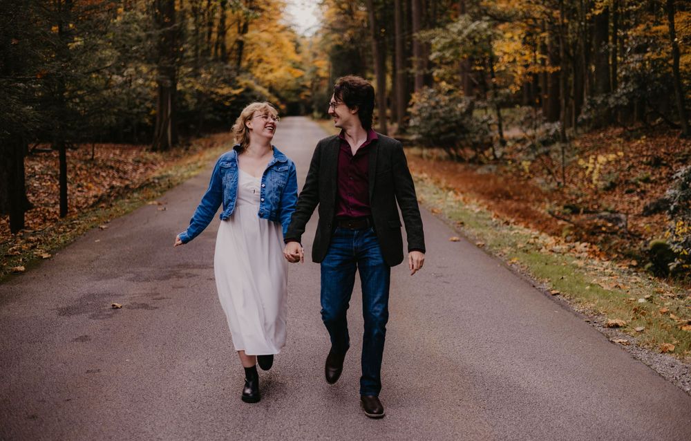 Happy couple walks hand in hand down a tree-lined autumn road with colorful fall foliage.