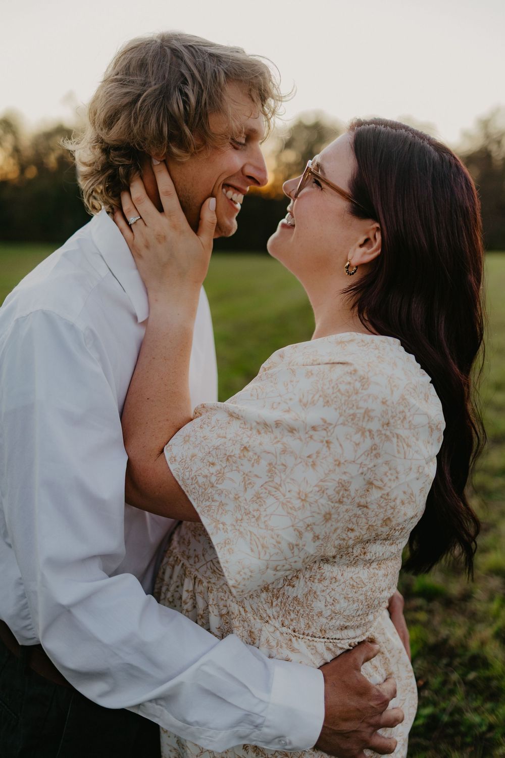 Smiling couple gazing at each other at sunset in a green field, woman touching mans face.