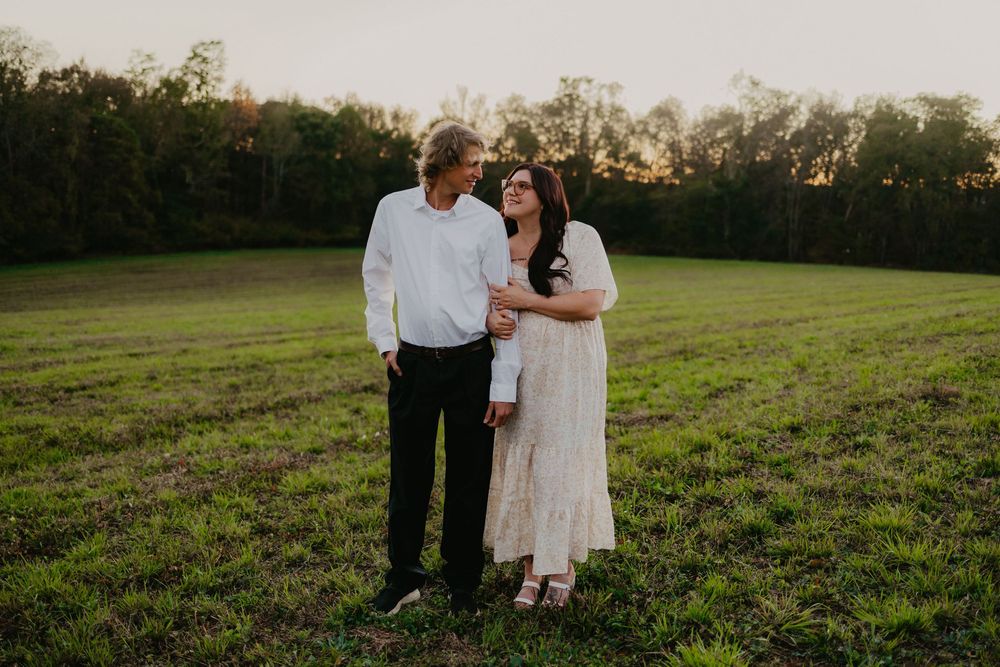Couple shares a tender moment smiling at each other in an open green field at golden hour.