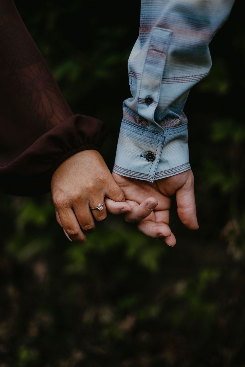 Close-up of two people holding hands, one wearing a diamond engagement ring, symbolizing love and commitment.