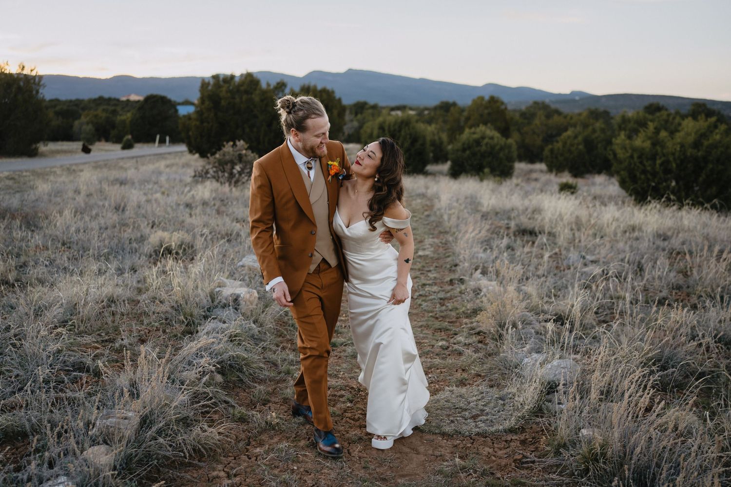 Bride and groom walk laughing through desert landscape in golden sunset light in New Mexico at Nature Pointe Venue