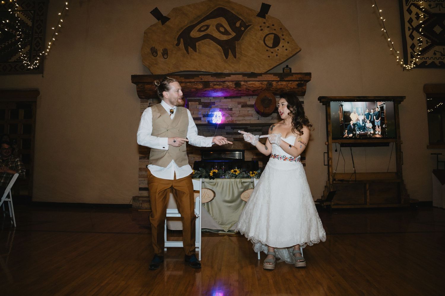 Bride and groom share a joyful first dance at rustic wedding reception with string lights backdrop.