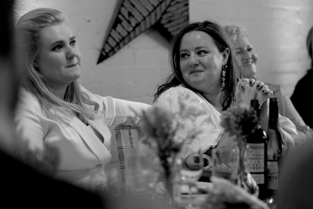 Two women in white blazers sit together at a table during a formal event in black and white photo.