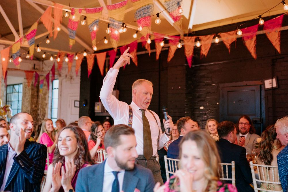 Guests celebrate at a festive wedding reception adorned with colorful bunting and string lights indoors.